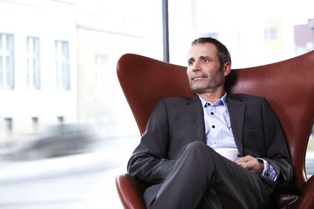 Business executive in red chair enjoying coffee.の写真素材