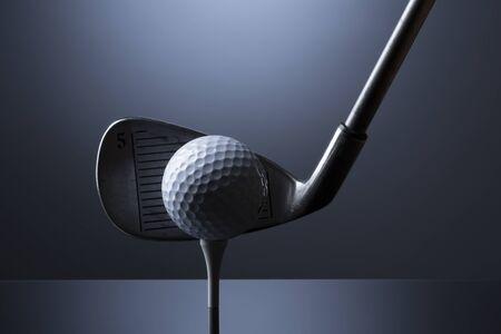 Golf ball on tee with club isolated on dark blue background.の写真素材