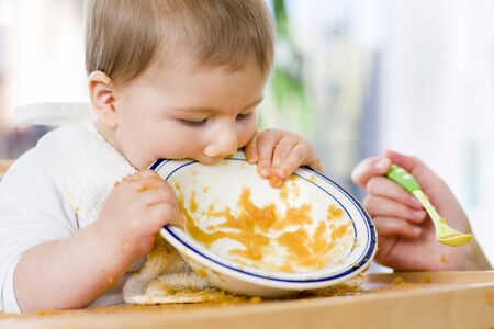 Sweet messy baby boy biting plate after eating the food.の写真素材