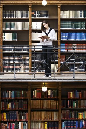 Woman reading in front of old bookshelf.の写真素材