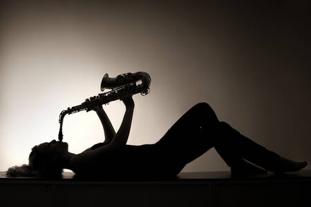 Silhouette of lying woman playing saxophone, sepia toned.の写真素材