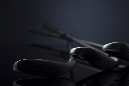 Close up of golf clubs lying on dark reflective surface.