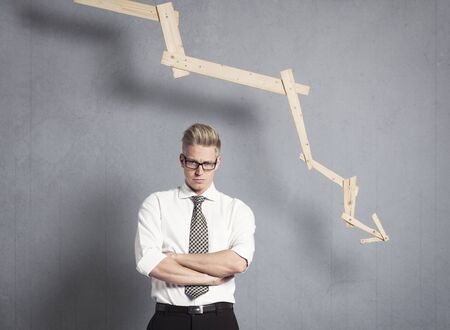 Displeased businessman in front of graph with negative trend.の写真素材