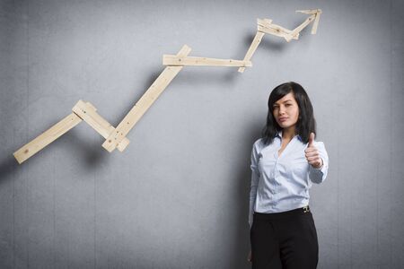 Pretty businesswoman holding thumb up in front of positive business chart.の写真素材