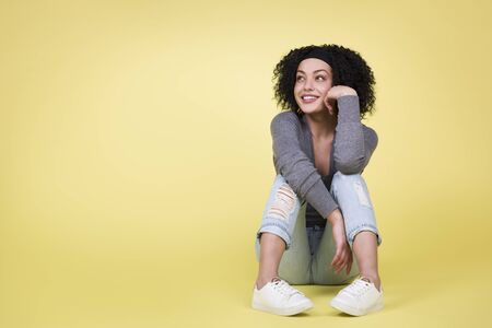 Joyful woman looking up sitting on isolated yellow background.の写真素材