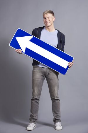 Smiling friendly man holding direction arrow sign pointing upwards with space for text isolated on grey background.の写真素材