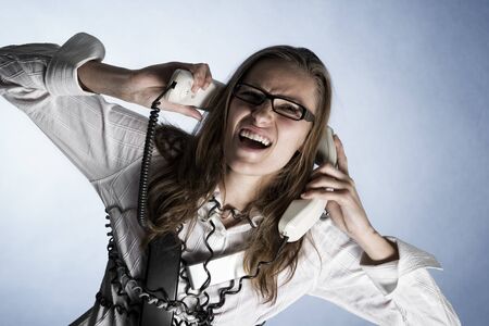 Furious telephonist in call center wrapped with phone cables being overstrained with work, isolated on blue background.の写真素材