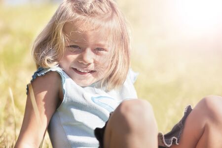 Portrait of joyfully smiling little girl sitting outdoors in grass.の写真素材