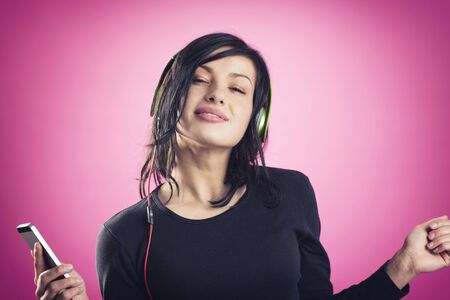 Smiling happy girl enjoying listening to music with earphones and mp3 player while dancing, isolated on pink background.の写真素材