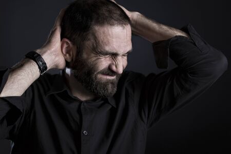 Devastated man throwing hands up, looking profoundly despaired, isolated on black background.の写真素材