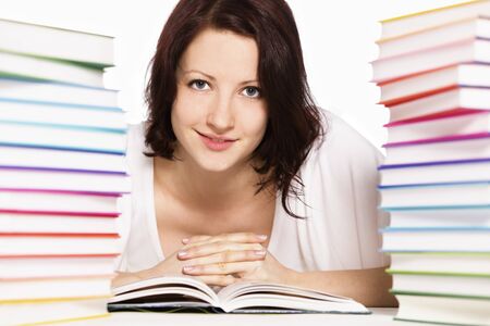 Close up of pretty smiling girl lying on floor between two stacks of colorful books reading and looking straight, isolated on white background.の写真素材
