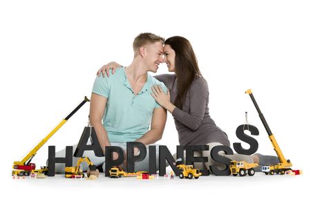 Developing happiness concept: Loving young couple along with construction machines building the word happiness, isolated on white background.の写真素材