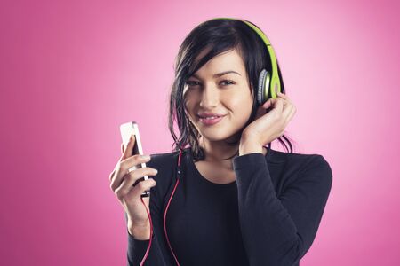 Smiling happy girl enjoying listening to music with headphones and mp3 player, isolated on pink background.の写真素材