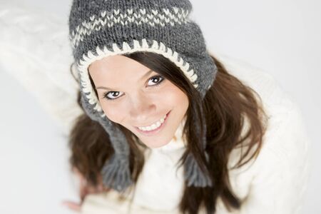 Close up of sweet young girl in winter pullover and cap, looking up with a charming smile on her face, isolated on grey background.の写真素材