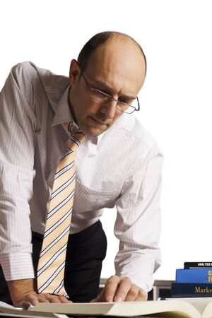 Male professional leaning over office desk studying business books and papers for new concepts.の写真素材