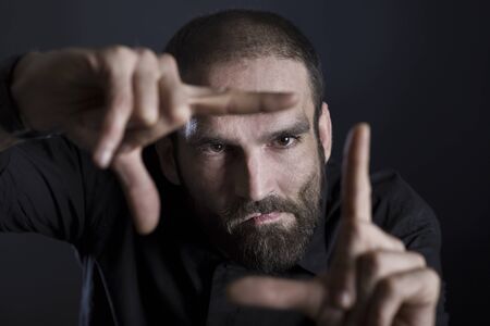 Serious focused man showing frame with fingers, isolated on black background.の写真素材