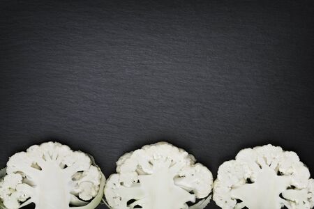 Three sliced white cauliflowers isolated on a dark grey stone slab with empty copy space.の写真素材