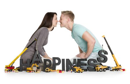 Creating happiness concept: Cheerful young man and woman along with construction machines building the word happiness, isolated on white background.の写真素材