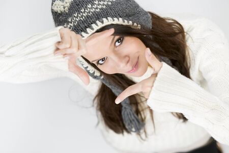 Charming young woman in warm winter clothes, making a photo frame with her hands while looking up...