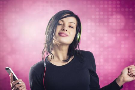 Smiling happy girl enjoying listening to music with headphones and mp3 player while dancing, isolated on pink disco background.の写真素材