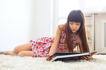 Charming little girl reading book on white carpet aの写真素材