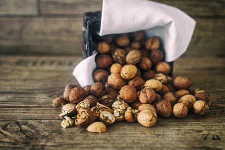 Fresh walnuts spill out of a wicker basket on autumn background on the old wooden table, selective...