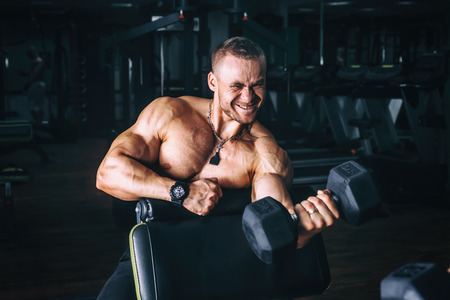 very power athletic guy bodybuilder , execute exercise with dumbbells, in dark gymの写真素材