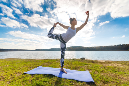 Young woman doing yoga near lake outdoors, meditation. Sport fitness and exercising in nature, autumn sunsetの写真素材