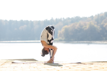 Young woman doing yoga near lake outdoors, meditation. Sport fitness and exercising in nature, autumn sunsetの写真素材