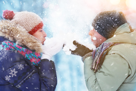 Happy Young Couple in Winter Park blowing snow. laughing and having fun. Family Outdoors.の写真素材