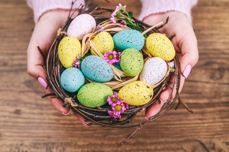 Woman hands holding painted easter egg in a small nest. Toned picture. Top view. Selective focus.の写真素材
