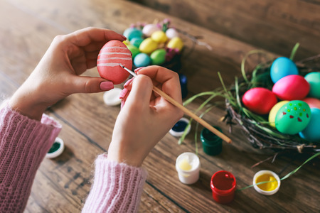 Female hands painting Easter eggs on dark wooden table. Toned picture. Selective focus.の写真素材