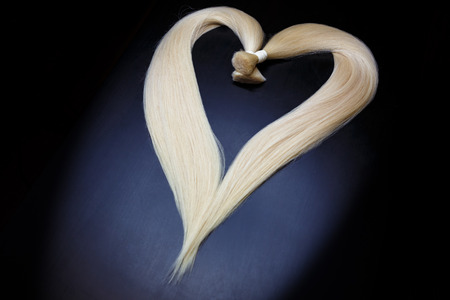 hair extension equipment of natural blonde hair. heart shape on a dark background.の写真素材