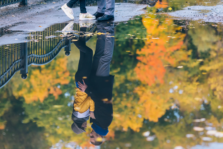 Young people in autumn park. Reflection in a puddle. Yellow Trees and Leaves. Happy young family concept.の写真素材