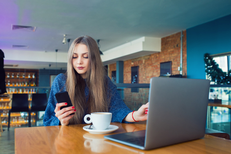 Woman typing text message on smart phone in a cafe. Cropped image of young woman sitting at a table with a coffee using mobile phone.の写真素材