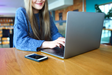 Woman working on laptop in a cafe. Young woman sitting at a table with a coffee usinglaptop. With blank copy space scree for your advertising text message or promotional content Toned image. Selective focus.の写真素材
