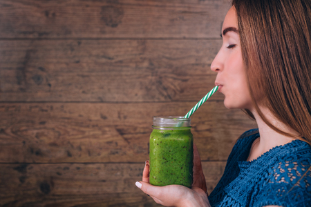 Woman holding kiwi smoothie. Healthy lifestyle concept. Dark wooden background.の写真素材