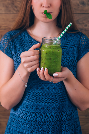 Woman holding kiwi smoothie. Healthy lifestyle concept. Dark wooden background.の写真素材