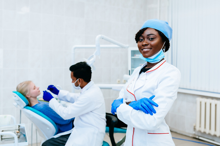 Young smiling African american female dentist in front of dentist checking teeth to patient at clinic. Dental clinic concept.の写真素材