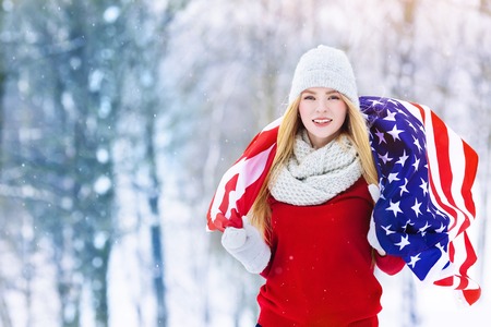 Winter portrait of young teen girl with USA flag. Beauty Joyful Model Girl laughing and having fun in winter park. Beautiful young woman outdoors. Enjoying nature, wintertimeの写真素材