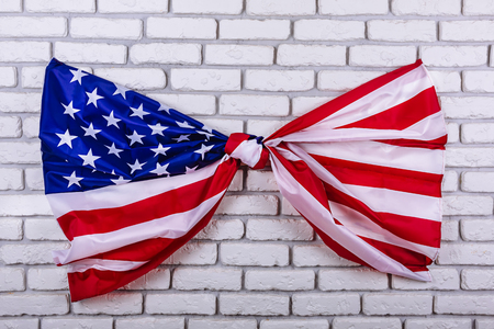 American flag, tied in a knot, on a white brick wall. Visual concept of preparation for Independence Day. Fourth of July patriotic consept.の写真素材