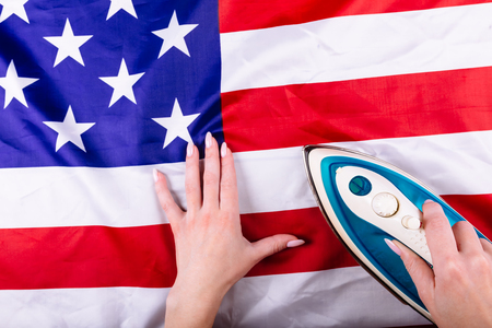 Woman hands pressing American Flag with an iron. Visual concept of preparation for Independence Day. Fourth of July patriotic consept.の写真素材