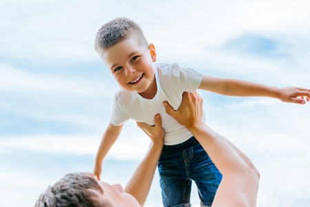 Father throwing his little son up in the air. Family time together. Happy little boy having fun with his dad outdoorsの写真素材
