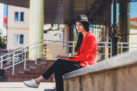 Happy hipster young woman working on laptop outdors. Student girl using laptop in university campus. Toned image.の写真素材
