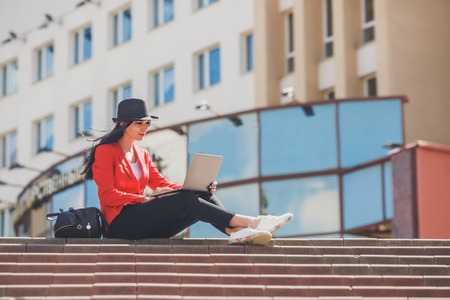 Happy hipster young woman working on laptop outdors. Student girl using laptop in university campus. Toned image.の写真素材