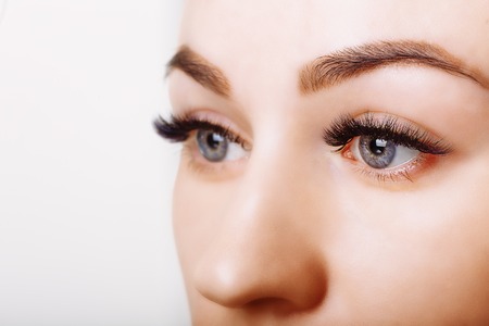 Eyelash extension procedure. Woman eye with long eyelashes. Close up, selective focus.