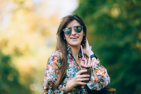 Young woman in sunglasses with milkshake. Outdoor autumn lifestyle portrait of pretty smiling female.の写真素材