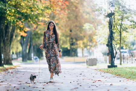 Young woman in sunglasses walking in autumn park with little puppy. Outdoor lifestyle portrait of pretty smiling female and her small dog.の写真素材