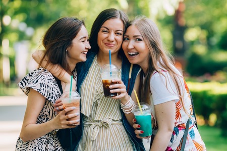 Summer lifestyle portrait multiracial women enjoy nice day, holding glasses of milkshakes. Happy friends in the park on a sunny day. Best friends girls having fun, joy. Lifestyle. Asian, jewess and caucasian.の写真素材