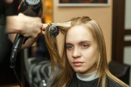 Professional hairdresser dyeing hair of her client in salon. Haircutter dry hair with hairdrier. Selective focus.の写真素材